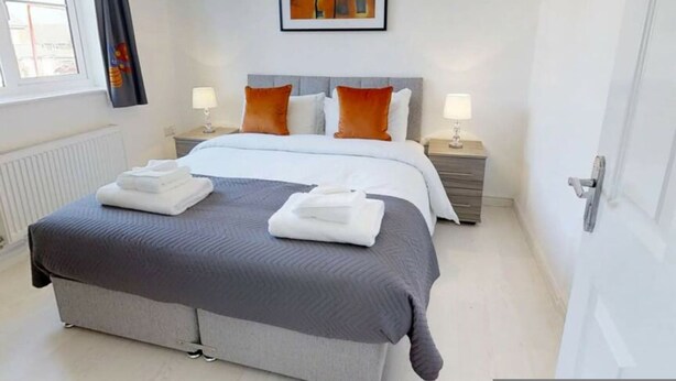A hotel room with a bed, two bedside tables, a window, a radiator, and a painting on the wall. - Cole Green Lane Executive Stay- Free Parking (Welwyn Garden City)