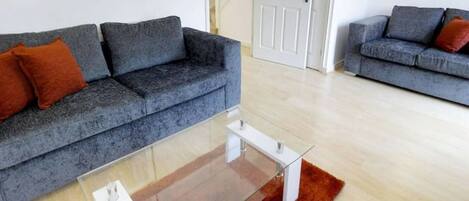 A living room with two grey sofas, a glass coffee table, and a wooden floor.