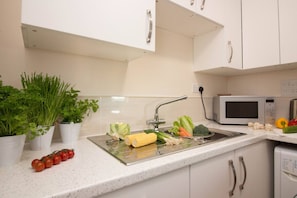 A kitchen with a stainless steel sink, white cabinets, a microwave, and various vegetables on the counter. - Castle Point Apartments Southampton 19 (Southampton)