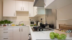 Una cocina con armarios blancos, microondas, tostadora, estufa y manzanas verdes sobre la encimera.