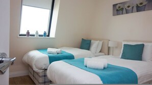 Habitación de hotel con dos camas, una ventana con botellas en el alféizar y un cuadro de flores en la pared.