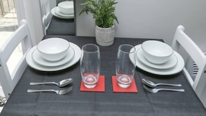 A dining table set with white plates, clear glasses, and silverware on a dark tablecloth, with a potted plant on the table. - Modern London Studio 15mins to Central London (London)