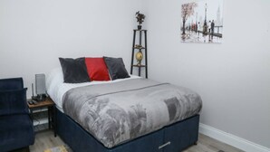 A bedroom with a bed, bedside table, lamp, chair, and a painting on the wall. - Modern London Studio 15mins to Central London (London)
