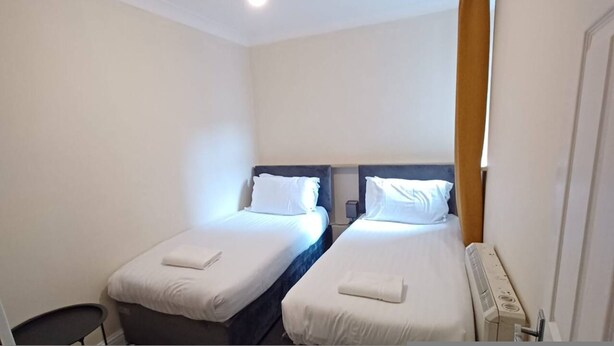 A hotel room with two single beds, a chair, a radiator, and a window with curtains. - Southampton 2-bedroom House (Southampton)