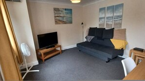 A living room with a sofa, a television, a fan, and artwork on the wall. - Southampton 2-bedroom House (Southampton)