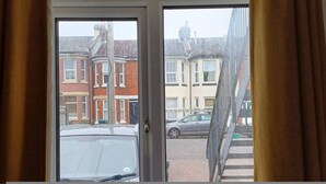 A view through a window with curtains, revealing a residential street with houses and parked cars. - Southampton 2-bedroom House (Southampton)