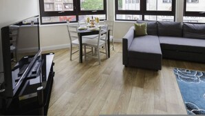 A modern living room with a grey sofa, a dining table with chairs, and a large window with a view of buildings. - Castle Point 6 Apartment - Premier Lodge (Southampton)
