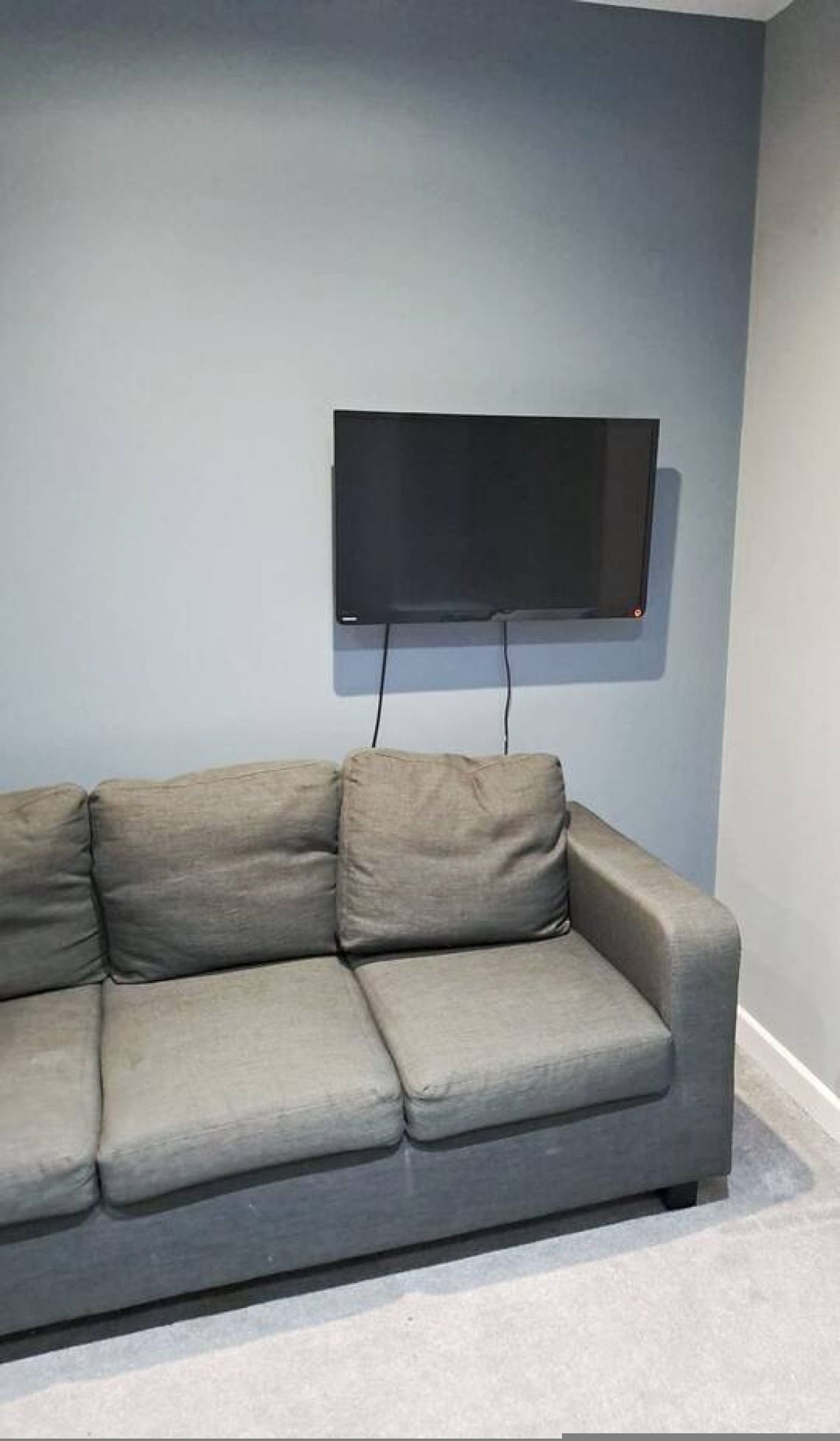 A gray sofa with a flat-screen TV mounted on the wall above it.