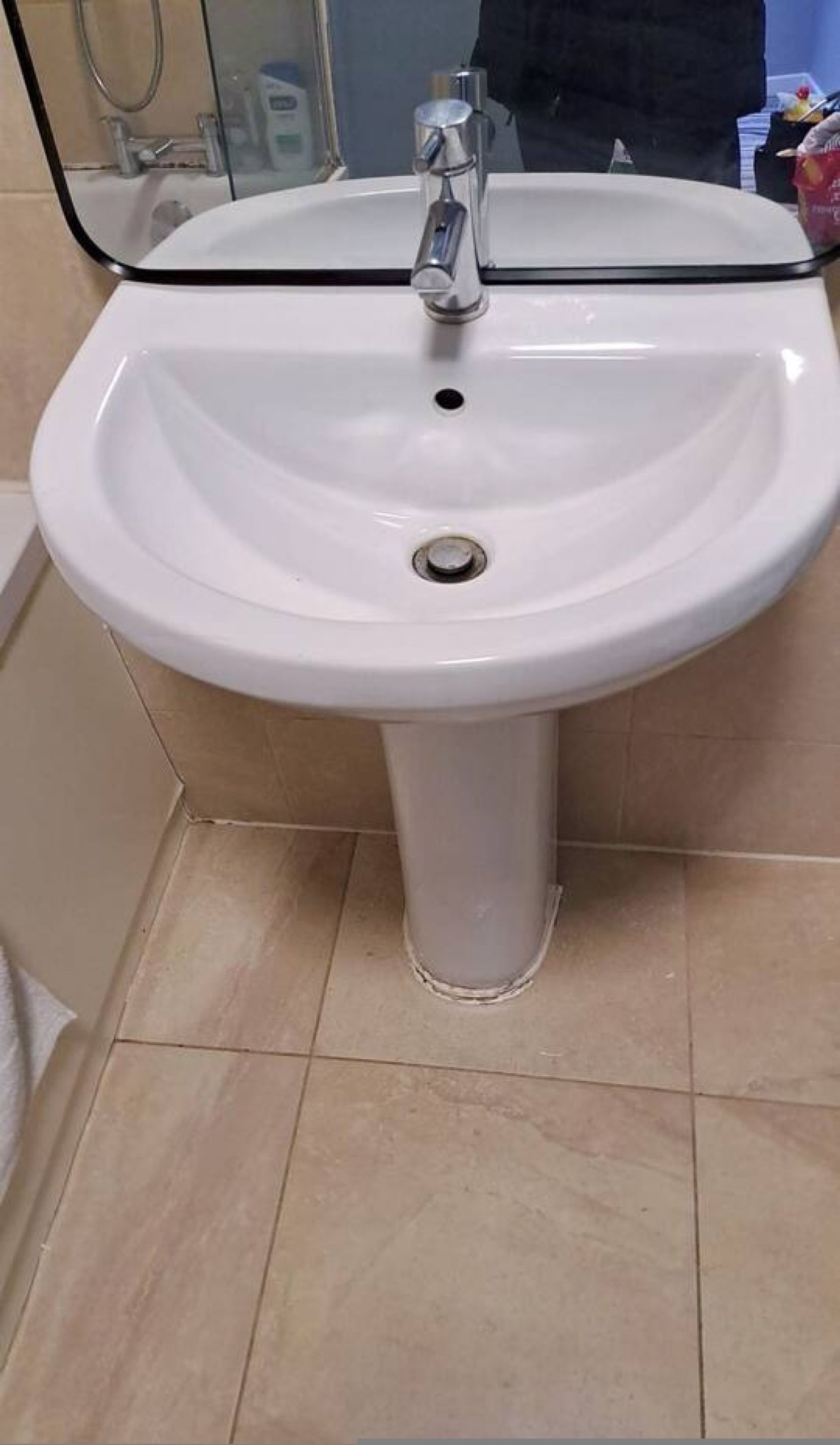 Egy fürdőszoba, melyben fehér, lábazatos mosdókagyló, tükör és zuhanyzó található.