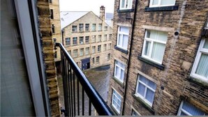 A multi-story building with a brick facade, multiple windows, and a visible balcony railing. - Bradford City Victorian Mill Escape Apartment 3 (Bradford)