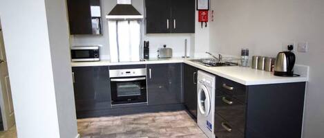A compact kitchen with a microwave, oven, and washing machine.