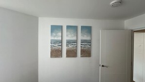 A bathroom with a white door, a white wall, and three vertical paintings depicting a beach scene. - Stylish Accommodation in Southampton 10 (Southampton)