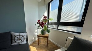 A room with a wooden floor, a window with blinds, a potted plant, and two sofas with cushions. - Stylish Accommodation in Southampton 10 (Southampton)