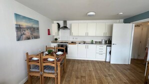 A compact kitchen with white cabinets, a dining table with chairs, and a wooden floor. - Stylish Accommodation in Southampton 10 (Southampton)