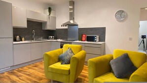 A modern kitchen with a microwave, toaster, and sink. There are two yellow armchairs with cushions. - Charming Bedford Apartment 1 Near Bedford Park (Bedford)