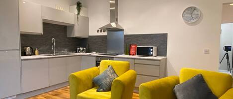 A modern kitchen with a microwave, toaster, and sink. There are two yellow armchairs with cushions.