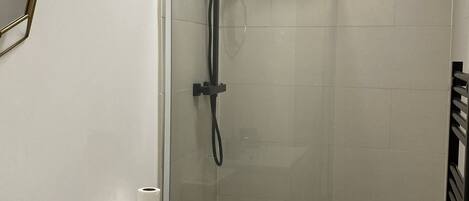 Eine Dusche mit Glastür, eine Toilette mit Papierhandtuchhalter und ein Seifenspender.