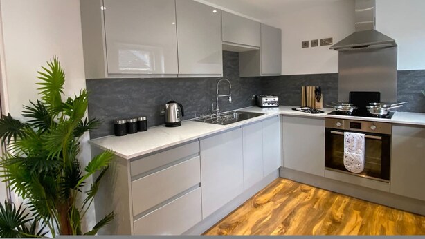 A modern kitchen with white cabinets, a stainless steel range hood, a built-in oven, and a wooden floor. - Stylish 2BR Serviced Apartment in Bedford Centre 4 (Bedford)