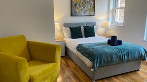 A bedroom with a bed, a yellow armchair, a painting on the wall, and a window. - Stylish 2BR Serviced Apartment in Bedford Centre 4 (Bedford)