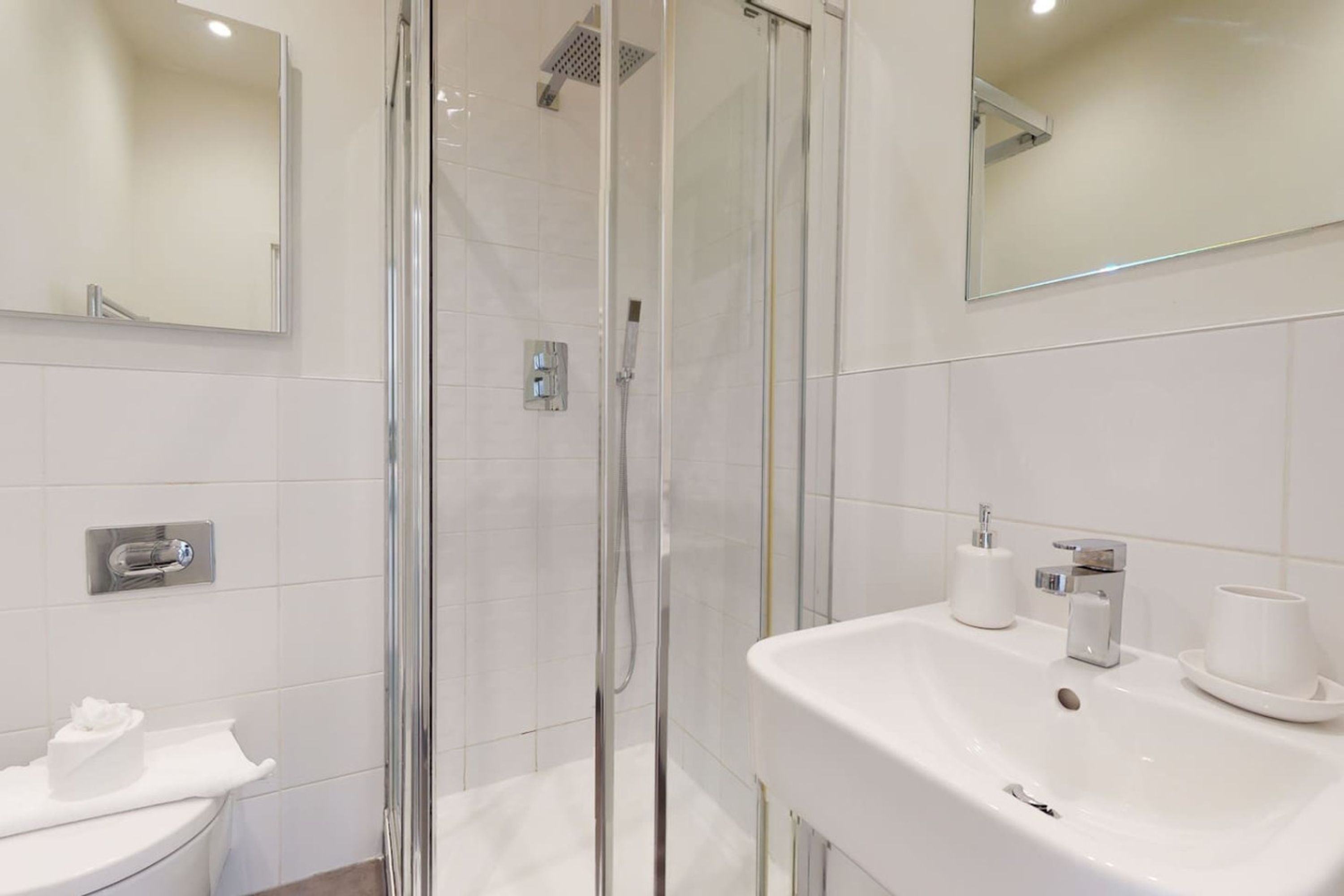 Et moderne badeværelse med et glasbadeværelse, en hvid vask med kop og sæbedispenser, samt et toilet.