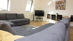 A modern living room with a grey sofa, a flat-screen TV, and a dining area with two chairs. - Premiere Serviced Accommodation - 17 (Southampton)