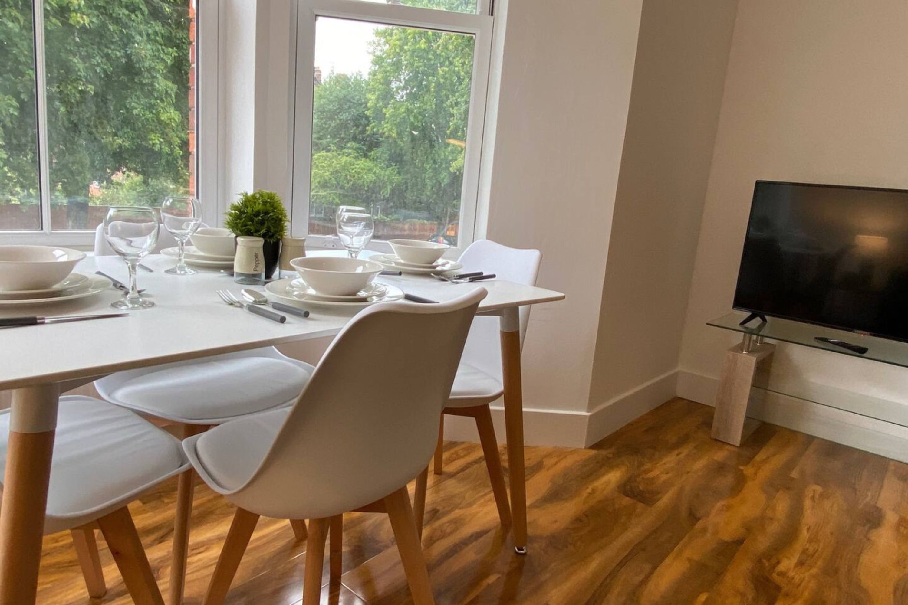 A dining area with a table set for four, a small potted plant, and a television on a stand.