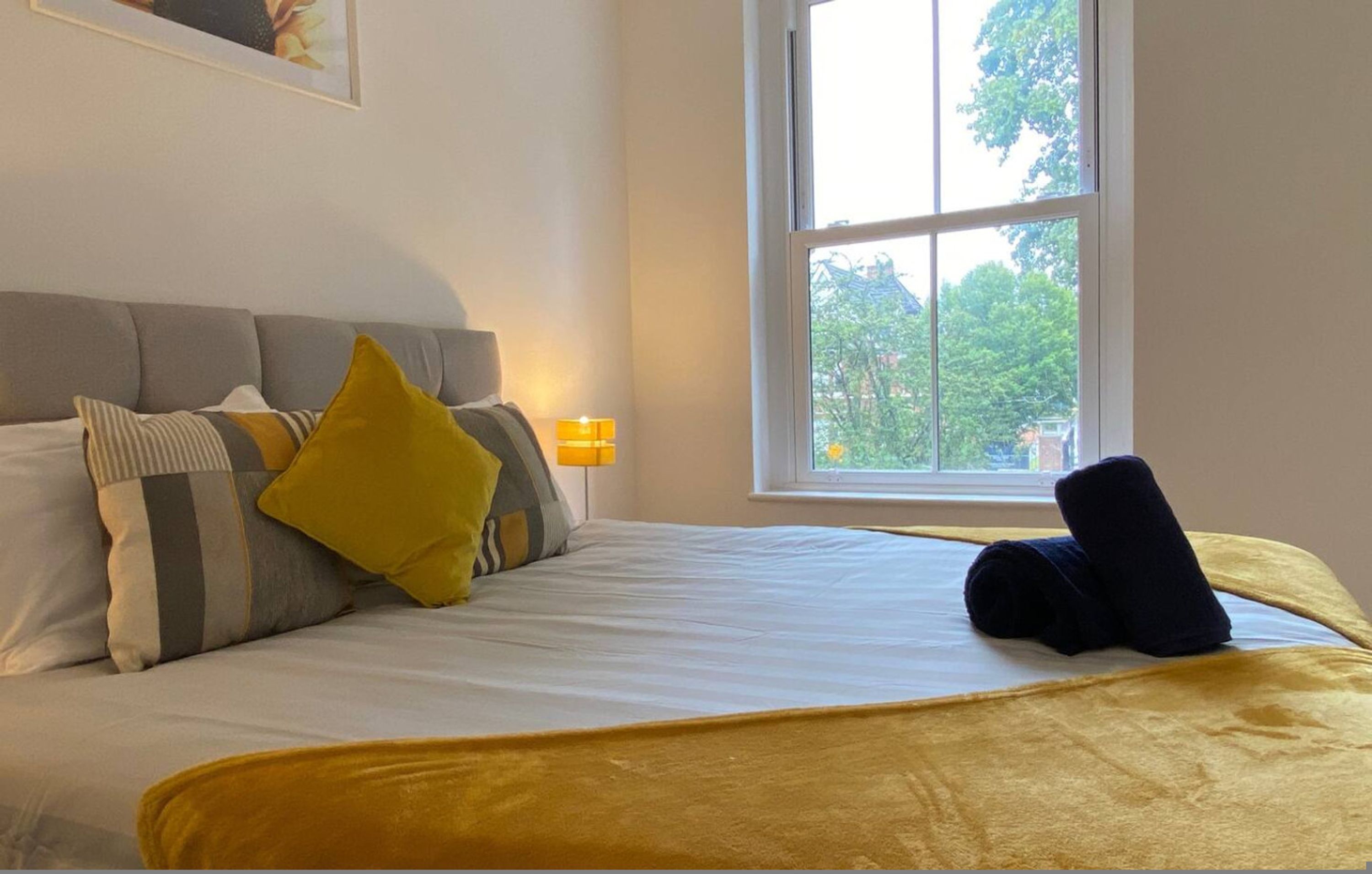 A neatly made bed with a yellow blanket, a grey and striped pillow, and a black pillow.