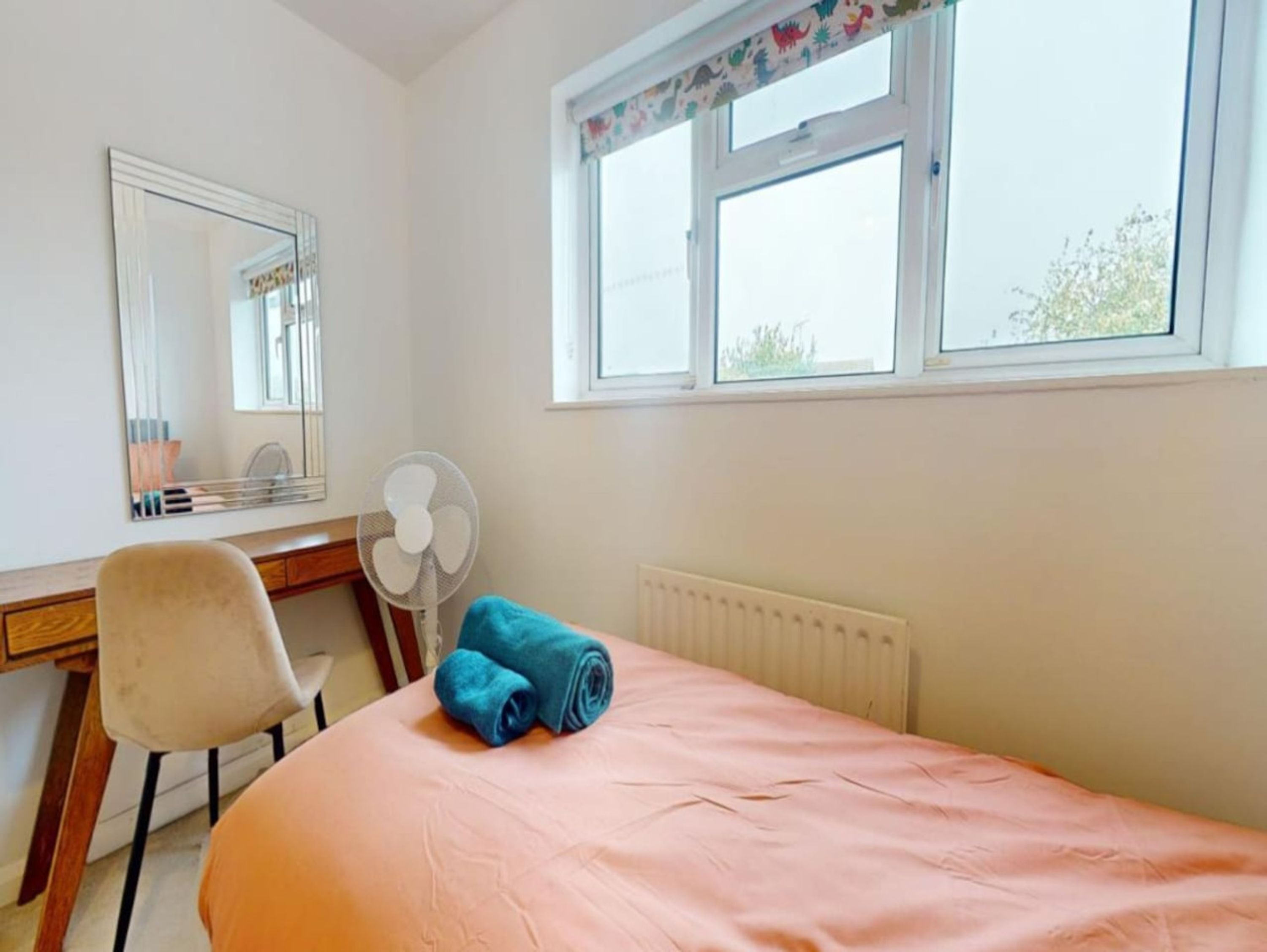 Een slaapkamer met een bed, een bureau, een stoel, een radiator en een raam met uitzicht.