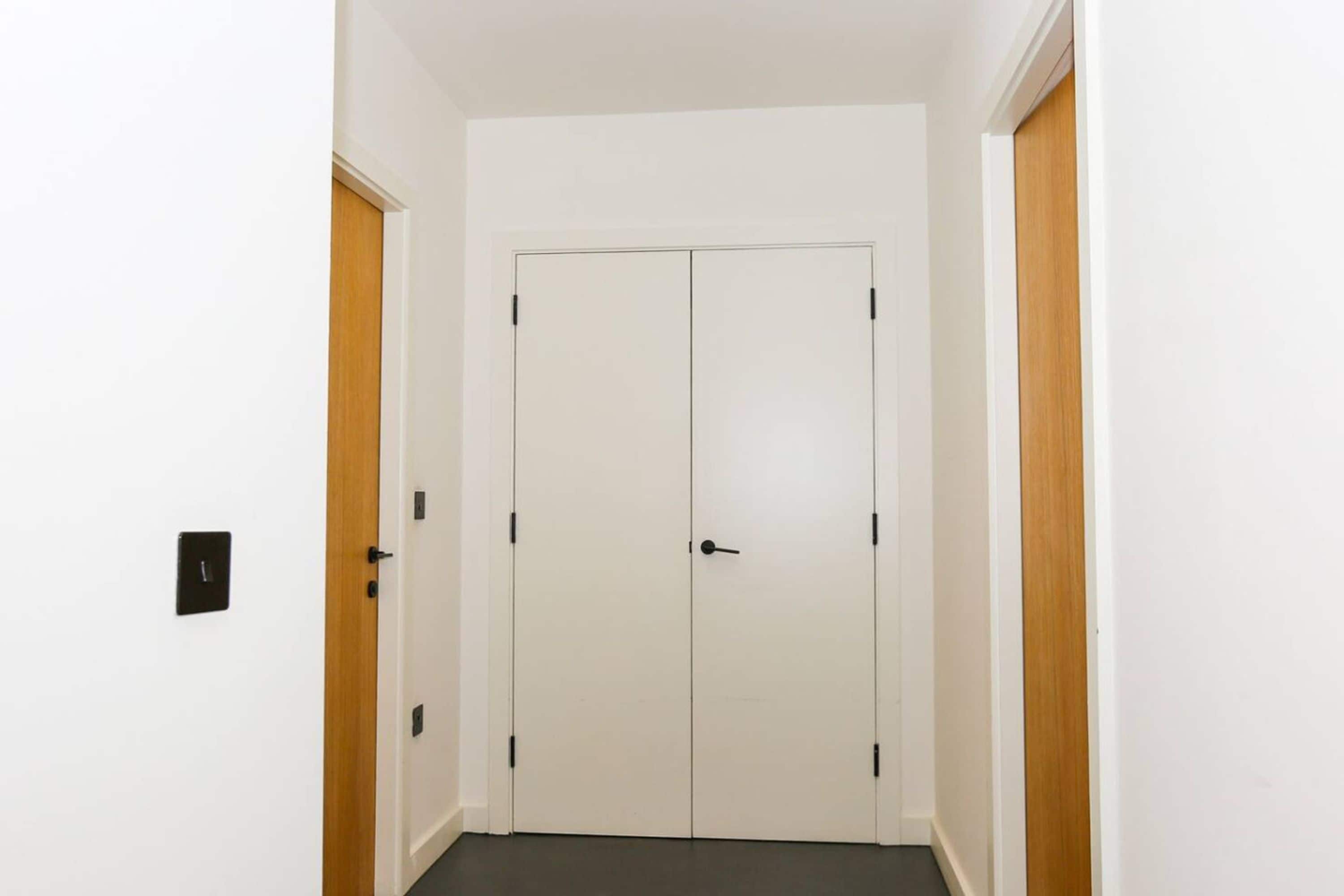 Un pasillo con una puerta doble, un interruptor de luz y detalles de madera en las paredes.