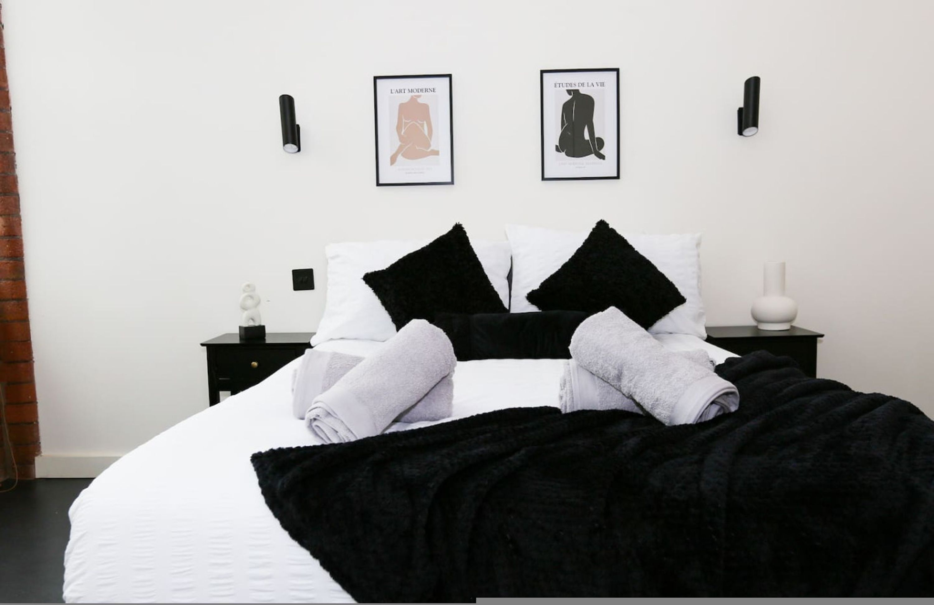A neatly made bed with black and white pillows, a black throw blanket, and two framed pictures on the wall.