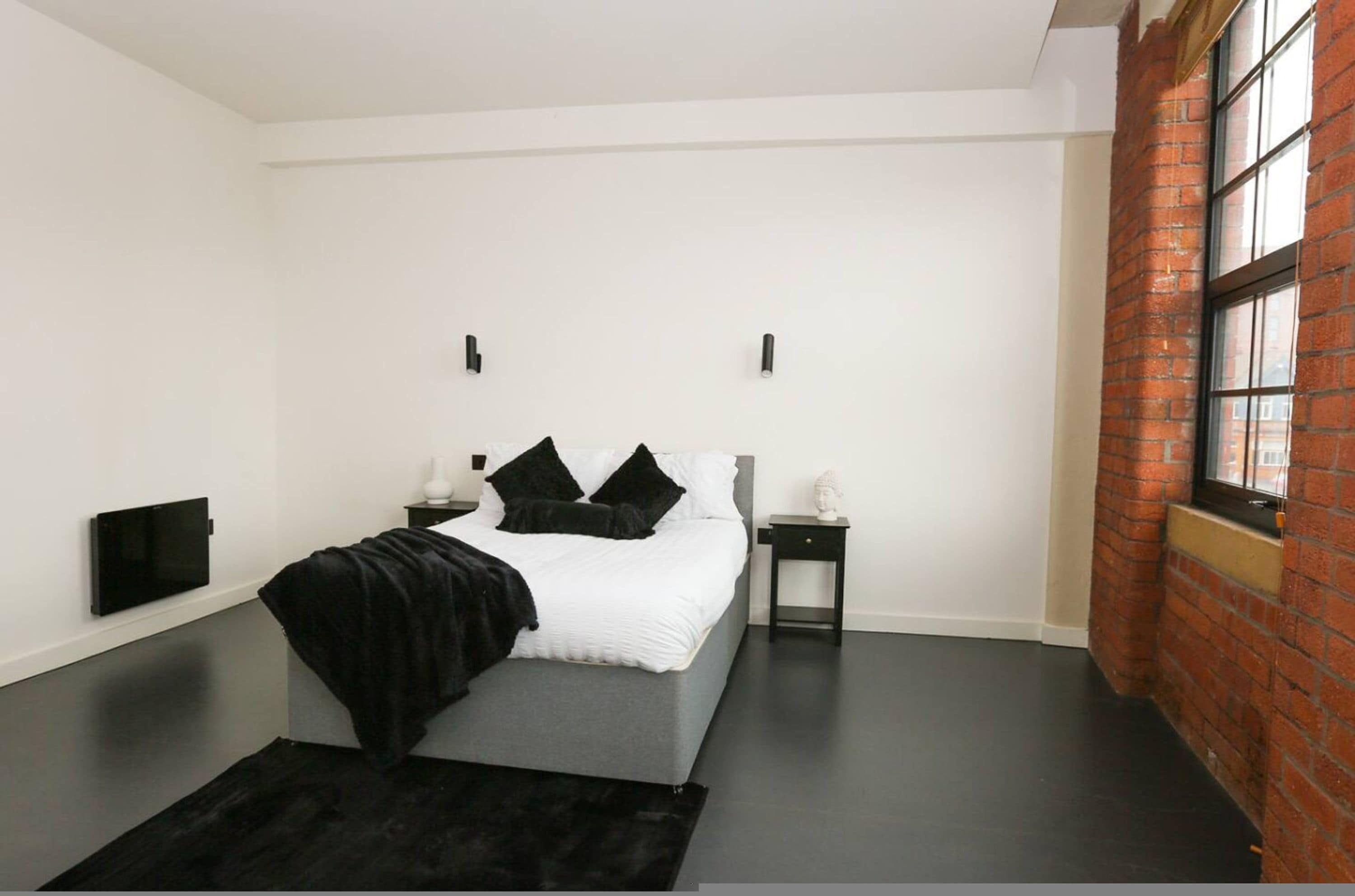 Une chambre à coucher moderne avec un lit, des tables de chevet, un téléviseur à écran plat et un mur en briques.