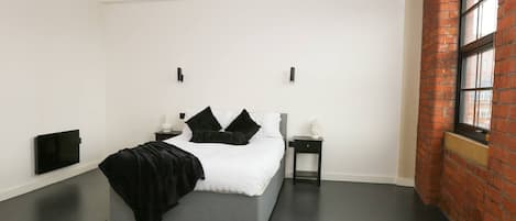 A modern bedroom with a bed, bedside tables, a flat-screen TV, and a brick wall.