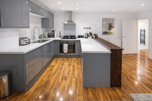 A modern kitchen with grey cabinets, a central island, stainless steel appliances, and a wooden floor. - Stylish Bedford Town Centre Apartment 5 Sleeps 6 Fast Wi-fi (Bedford)