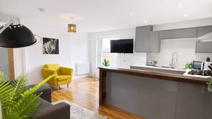 A modern kitchen with a central island, grey cabinets, a flat-screen TV, and a yellow armchair. - Stylish Bedford Town Centre Apartment 5 Sleeps 6 Fast Wi-fi (Bedford)