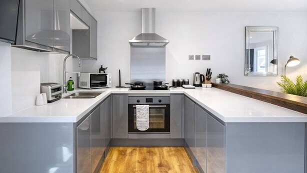 A modern kitchen with a central island, built-in oven, stainless steel range hood, and a large mirror above the countertop. - Stylish Bedford Town Centre Apartment 5 Sleeps 6 Fast Wi-fi (Bedford)