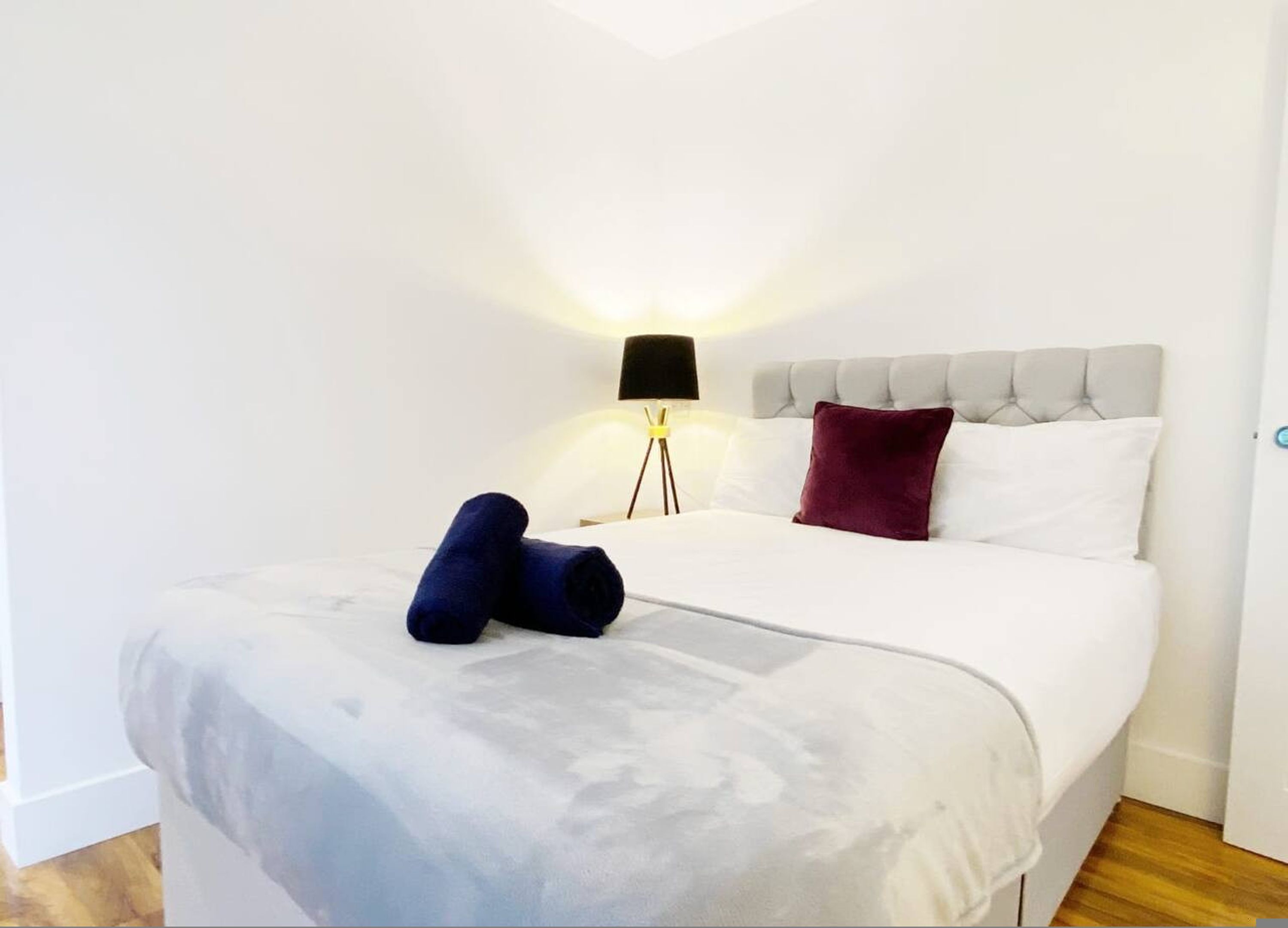 A neatly made bed with a grey headboard, white bedding, and a dark blue towel.