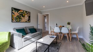 Una sala de estar moderna con un sofá gris, una mesa de centro y un comedor con una mesa y sillas.