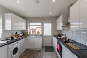 Una cocina compacta con armarios blancos, lavadora, lavaplatos y ventana.
