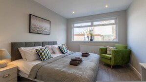 Un dormitorio con una cama, un sillón verde, una ventana con vistas y un radiador.
