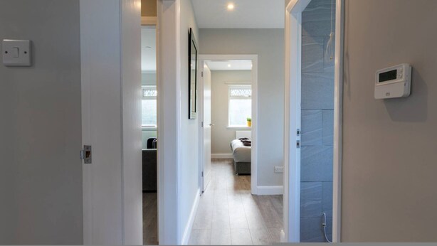 Un pasillo con una puerta que da a una habitación, un termostato en la pared y una ventana con persianas.