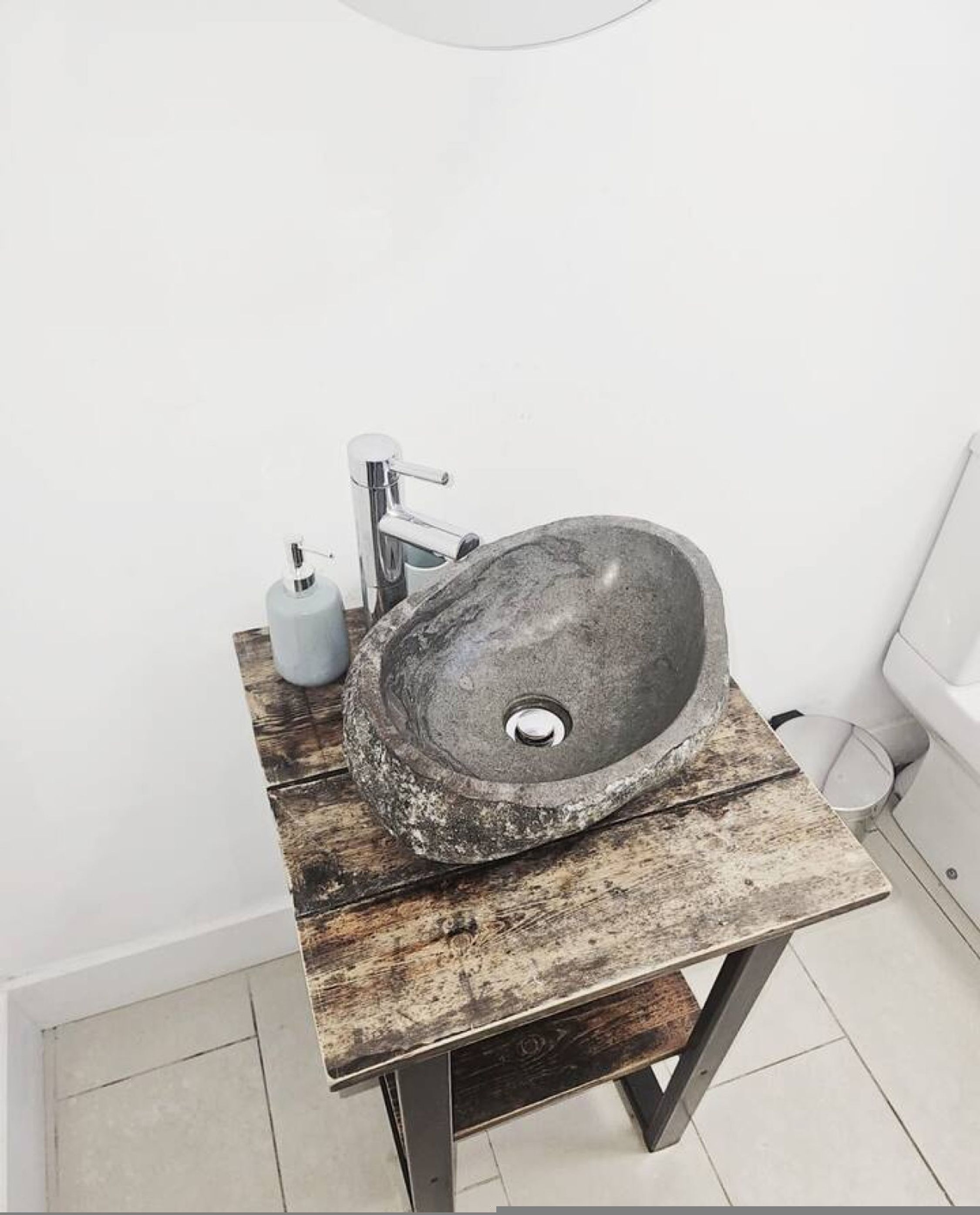 A bathroom with a stone sink, a wooden table, and a white wall.
