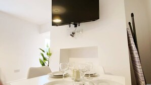 A dining area with a table set for four, a television mounted on the wall, and a plant in the background. - De Pary 2 Modern Bedford Apartment- Near Town Centre (Bedford)