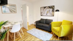A living room with a grey sofa, a yellow armchair, a white dining table with chairs, a white rug, and a painting on the wall. - De Pary 2 Modern Bedford Apartment- Near Town Centre (Bedford)