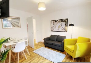 A living room with a grey sofa, a yellow armchair, a white dining table with chairs, a white rug, and a painting on the wall. - De Pary 2 Modern Bedford Apartment- Near Town Centre (Bedford)