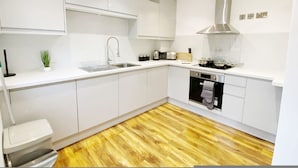A modern kitchen with white cabinetry, a stainless steel sink, a range hood, and a wooden floor. - De Pary 2 Modern Bedford Apartment- Near Town Centre (Bedford)