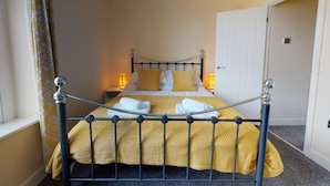 A neatly made bed with a metal frame, two bedside lamps, and a door to the right. - Westminster Luxe Stay City View 3BR Bradford (Bradford)