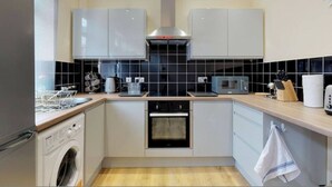 A modern kitchen with a washing machine, oven, microwave, and a coffee maker. - Westminster Luxe Stay City View 3BR Bradford (Bradford)