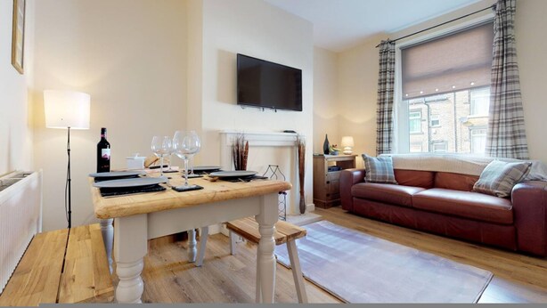A living room with a wooden table, a red leather sofa, a flat-screen TV, and a fireplace. - Westminster Luxe Stay City View 3BR Bradford (Bradford)