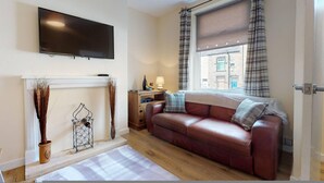 A living room with a sofa, a fireplace, a television, and a window with curtains. - Westminster Luxe Stay City View 3BR Bradford (Bradford)