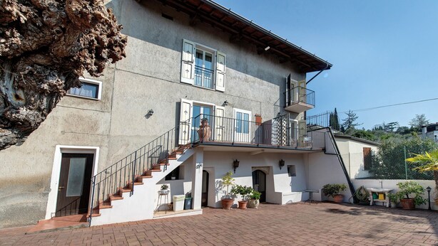 A two-story building with a staircase leading to a balcony, potted plants, and a paved courtyard. - Giardini Di Corte - Standard Bed and Breakfast with Lake View, Wi-Fi, and Air Conditioning (Toscolano Maderno)